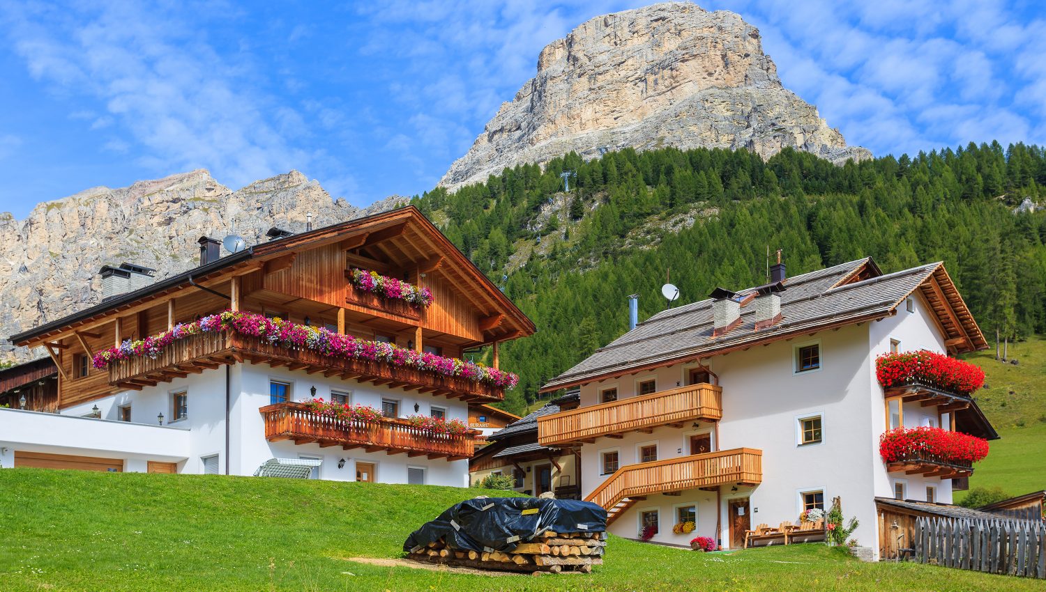 Houses in alpine village of Colfosco, Dolomites Mountains, Italy Traditional alpine houses with flowers on balcony in summer landscape of Dolomites Mountains (The Alps), Italy